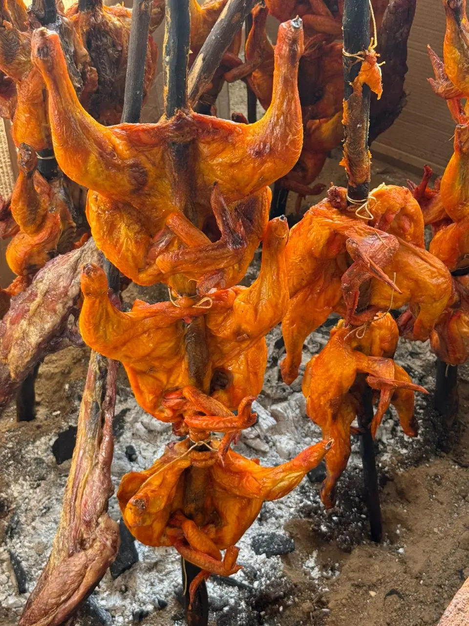 Asador de pollo en vara sobre carbón